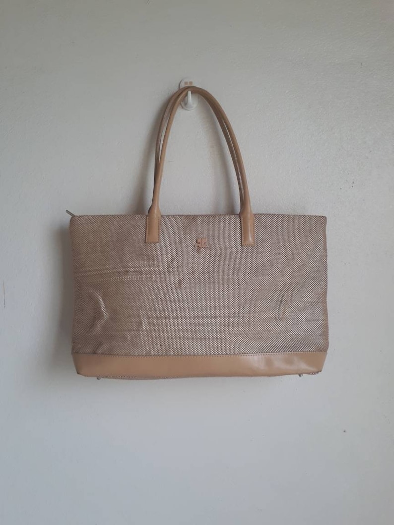 May include: A beige woven tote bag with leather handles and trim. The bag has a zipper closure and a small logo on the front.