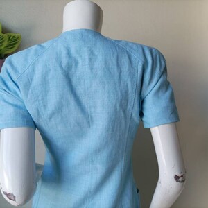 May include: A light blue linen blouse with short sleeves and a v-neck.