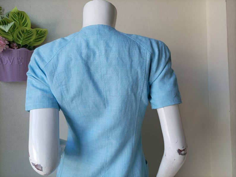 May include: A light blue linen blouse with short sleeves and a v-neck.