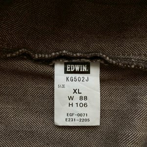 May include: Close-up of a brown herringbone fabric with a white tag. The tag reads "EDWIN" and includes size information: XL, W 88 inches, H 106 inches. The fabric has a textured appearance.