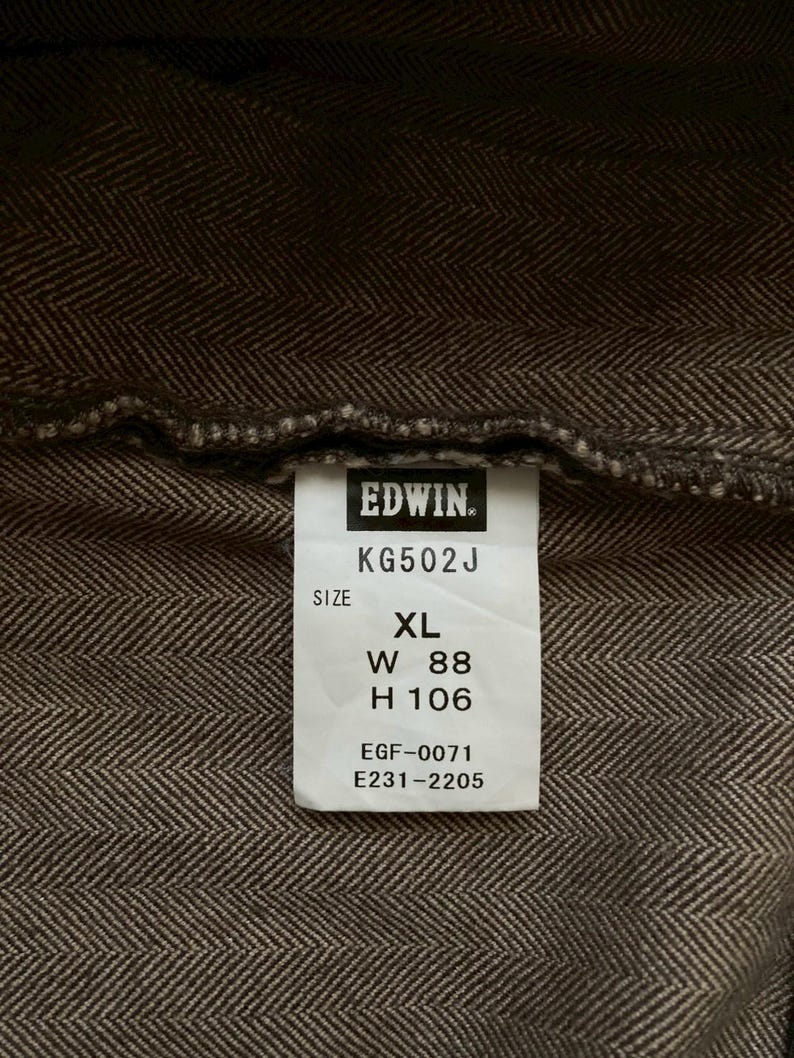 May include: Close-up of a brown herringbone fabric with a white tag. The tag reads "EDWIN" and includes size information: XL, W 88 inches, H 106 inches. The fabric has a textured appearance.