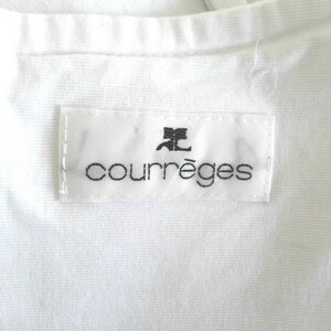 May include: White clothing label with black text that reads "Courr&egrave;ges" with a stylized letter "C" above the word.