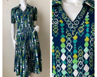 Puede incluir: Vestido vintage hasta la rodilla con cuello en V y mangas cortas. El vestido presenta un patrón geométrico en tonos de azul, verde y blanco. El vestido se exhibe en un maniquí, mostrando su ajuste y diseño.