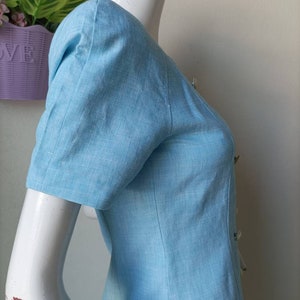 May include: A light blue linen dress with a button-up front and short sleeves. The dress has a slightly puffed sleeve detail.