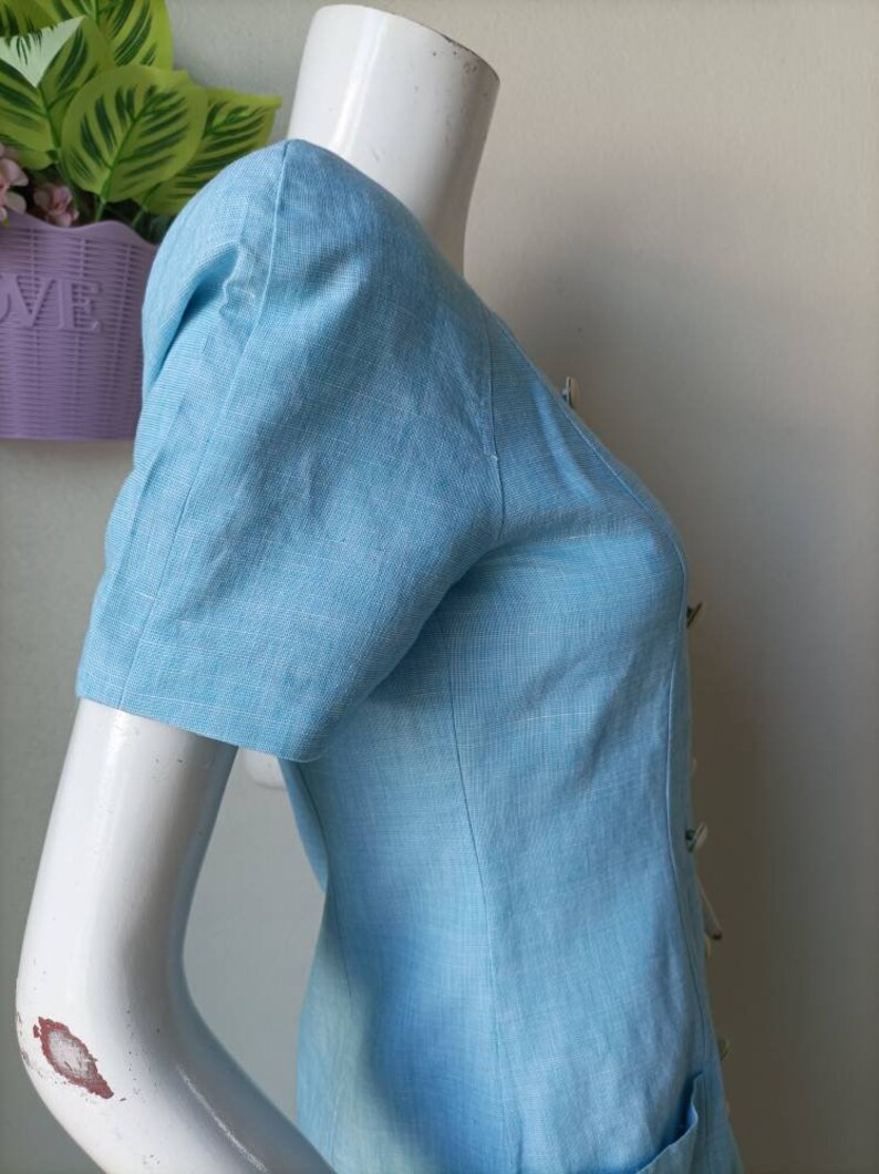 May include: A light blue linen dress with a button-up front and short sleeves. The dress has a slightly puffed sleeve detail.