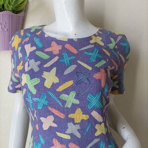 May include: A purple short-sleeved dress with a colorful abstract print of lines and crosses.