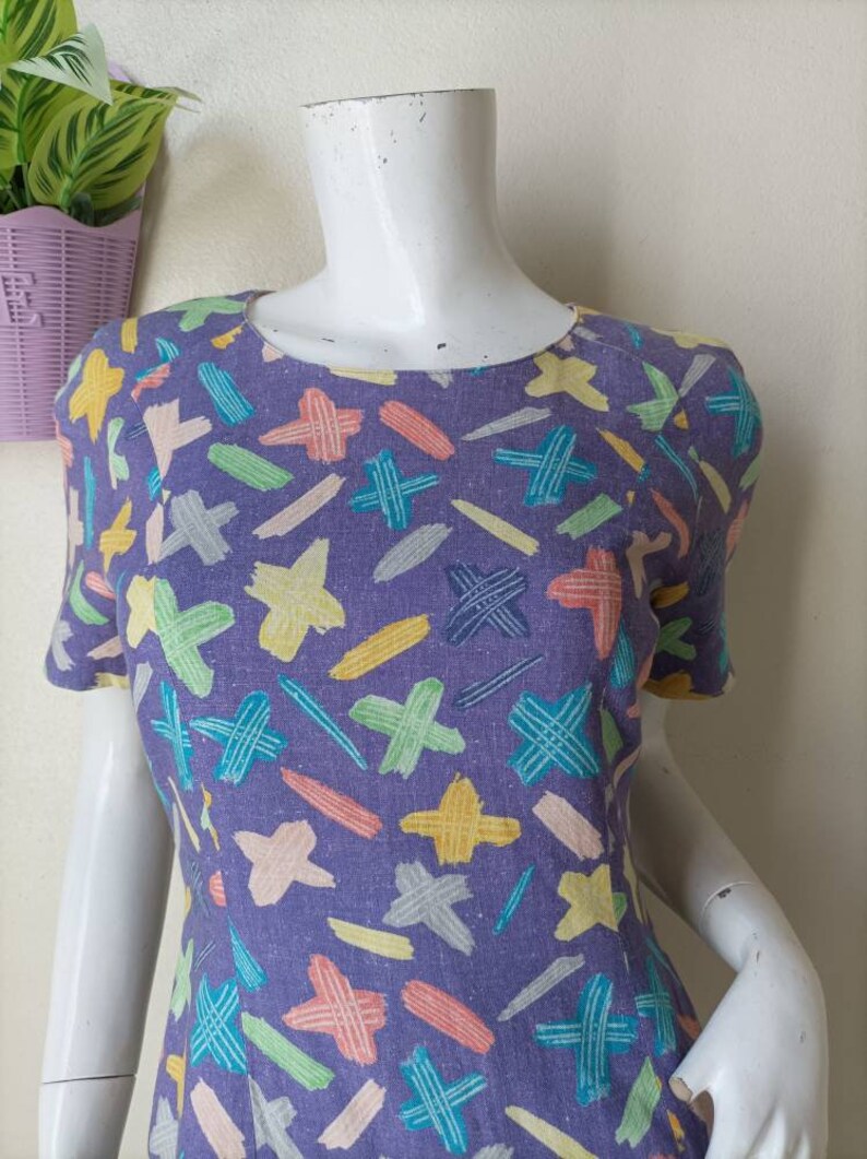 May include: A purple short-sleeved dress with a colorful abstract print of lines and crosses.