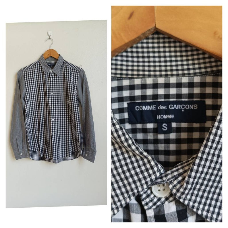 May include: A black and white checkered long-sleeve button-up shirt with a gray checkered pattern on the sleeves. The shirt has a label that reads "COMME des GAR&Ccedil;ONS HOMME S".
