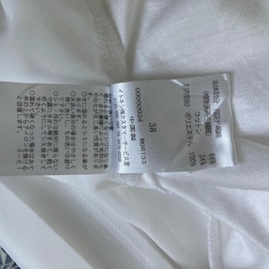 Peut inclure: Une &eacute;tiquette de tissu blanche avec du texte et des chiffres japonais, dont "38" et "MOR133". L'&eacute;tiquette indique la composition du tissu, avec des pourcentages de coton et de polyester. L'&eacute;tiquette est attach&eacute;e &agrave; un v&ecirc;tement blanc.