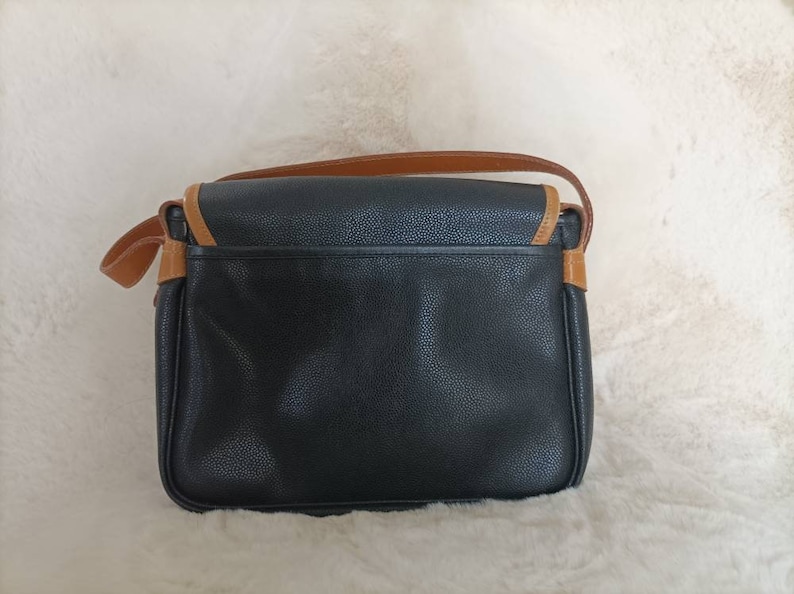 May include: A black leather shoulder bag with brown trim. The bag has a flap closure and a single strap.
