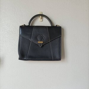 May include: A black leather satchel handbag with a gold clasp and a single handle.