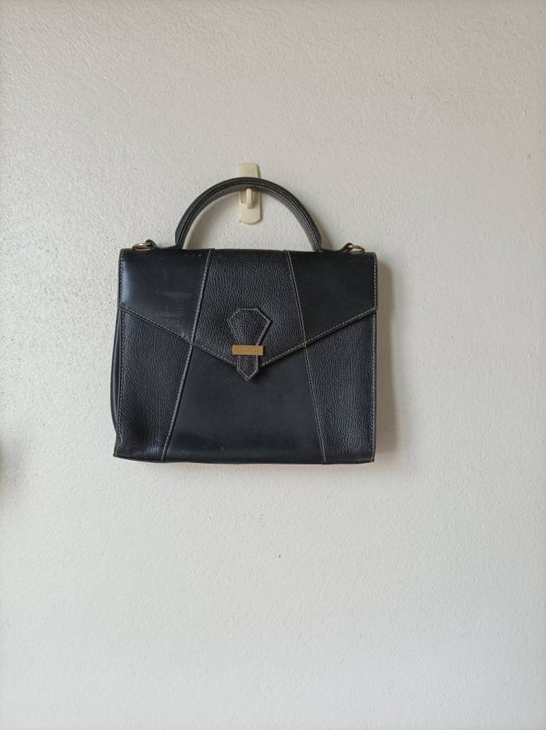 May include: A black leather satchel handbag with a gold clasp and a single handle.