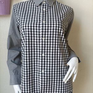 May include: A black and white checkered button-up shirt with long sleeves. The shirt has a small pocket on the left chest.