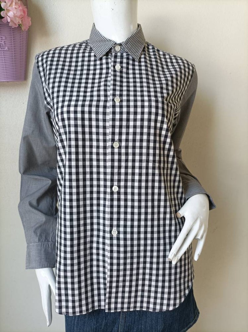May include: A black and white checkered button-up shirt with long sleeves. The shirt has a small pocket on the left chest.