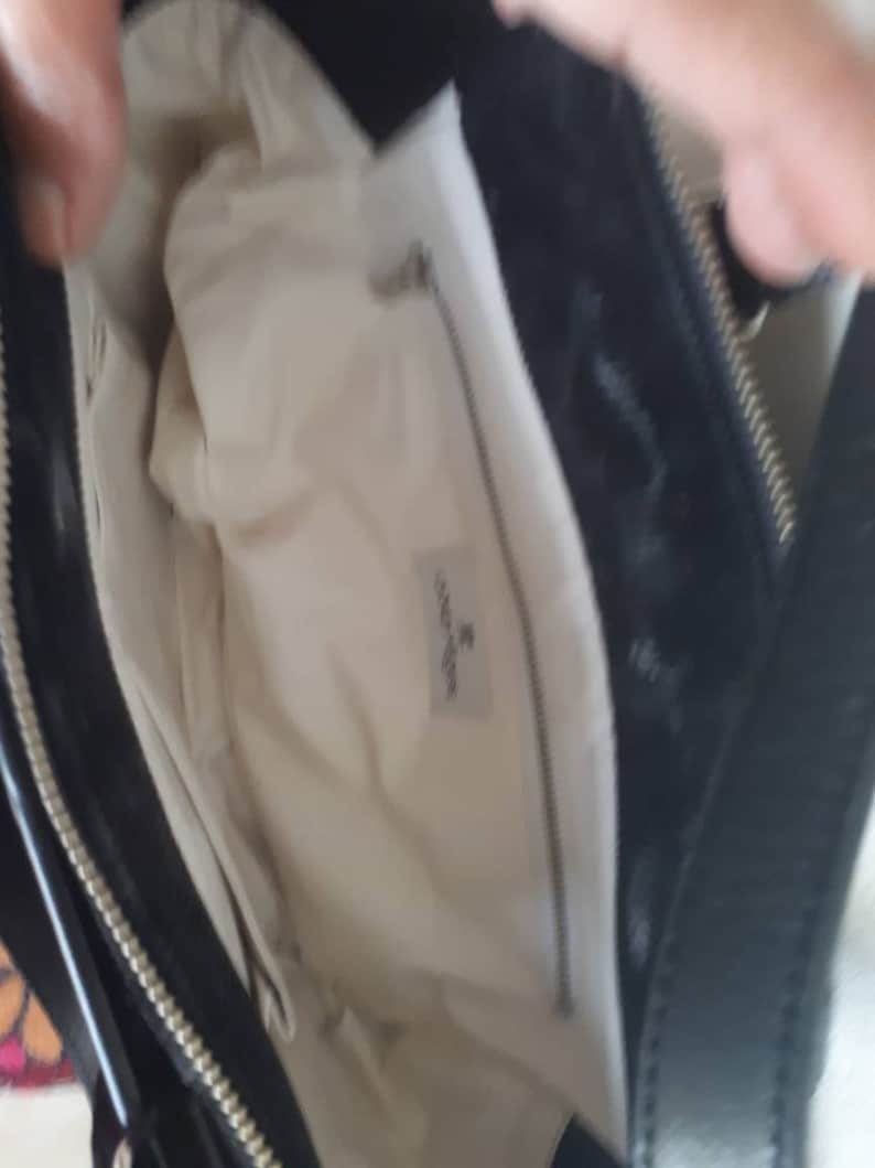 K&ouml;nnte beinhalten: Schwarze Ledertasche mit wei&szlig;em Stofffutter und Rei&szlig;verschluss. Das Futter hat ein kleines wei&szlig;es Etikett mit dem aufgedruckten Text "Coccinelle".