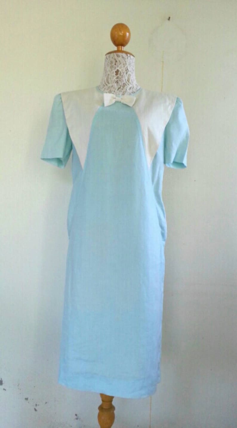 May include: A light blue dress with a white collar and a bow. The dress has short sleeves and a straight silhouette.
