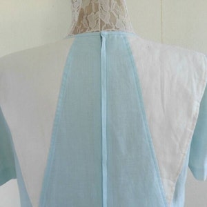 May include: A light blue dress with white panels on the shoulders and back. The dress has a V-neckline and short sleeves.