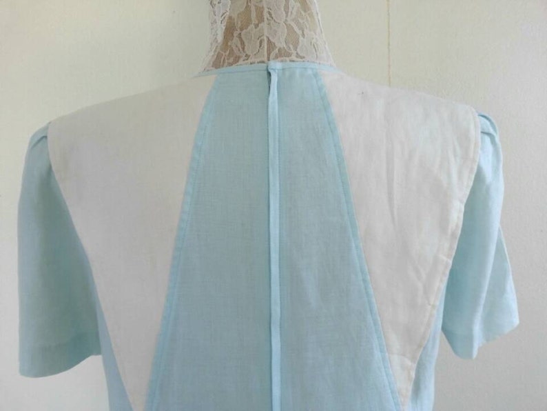 May include: A light blue dress with white panels on the shoulders and back. The dress has a V-neckline and short sleeves.