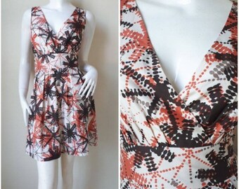 Op de afbeelding: Een mouwloze jurk met een V-hals en een witte achtergrond met een abstracte print in bruin, oranje en wit.
