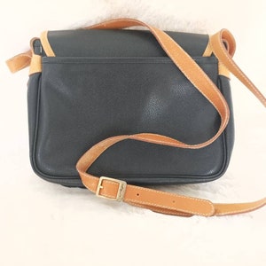 May include: A black leather shoulder bag with a brown leather strap and a gold buckle. The bag has a flap closure and a small pocket on the front.