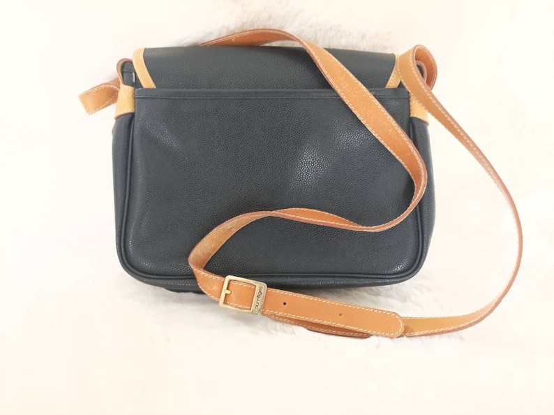 May include: A black leather shoulder bag with a brown leather strap and a gold buckle. The bag has a flap closure and a small pocket on the front.