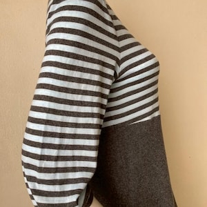 Puede incluir: Una blusa de manga tres cuartos con un dise&ntilde;o de bloques de color. Las mangas presentan rayas horizontales en azul claro y marr&oacute;n, mientras que el cuerpo es de color marr&oacute;n oscuro liso. La blusa se muestra en un maniqu&iacute;.