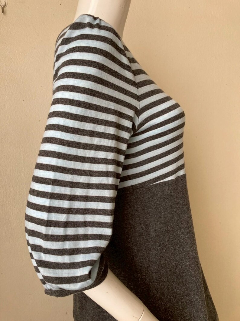 Puede incluir: Una blusa de manga tres cuartos con un dise&ntilde;o de bloques de color. Las mangas presentan rayas horizontales en azul claro y marr&oacute;n, mientras que el cuerpo es de color marr&oacute;n oscuro liso. La blusa se muestra en un maniqu&iacute;.