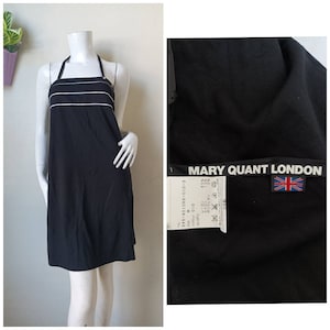 Könnte beinhalten: Schwarzes Halstuchkleid mit weißem Besatz und einem Mary Quant London-Etikett. Das Etikett trägt den Markennamen und eine Union Jack-Flagge.