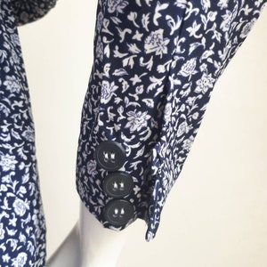 May include: A close-up of a navy blue and white floral patterned shirt sleeve with three black buttons.
