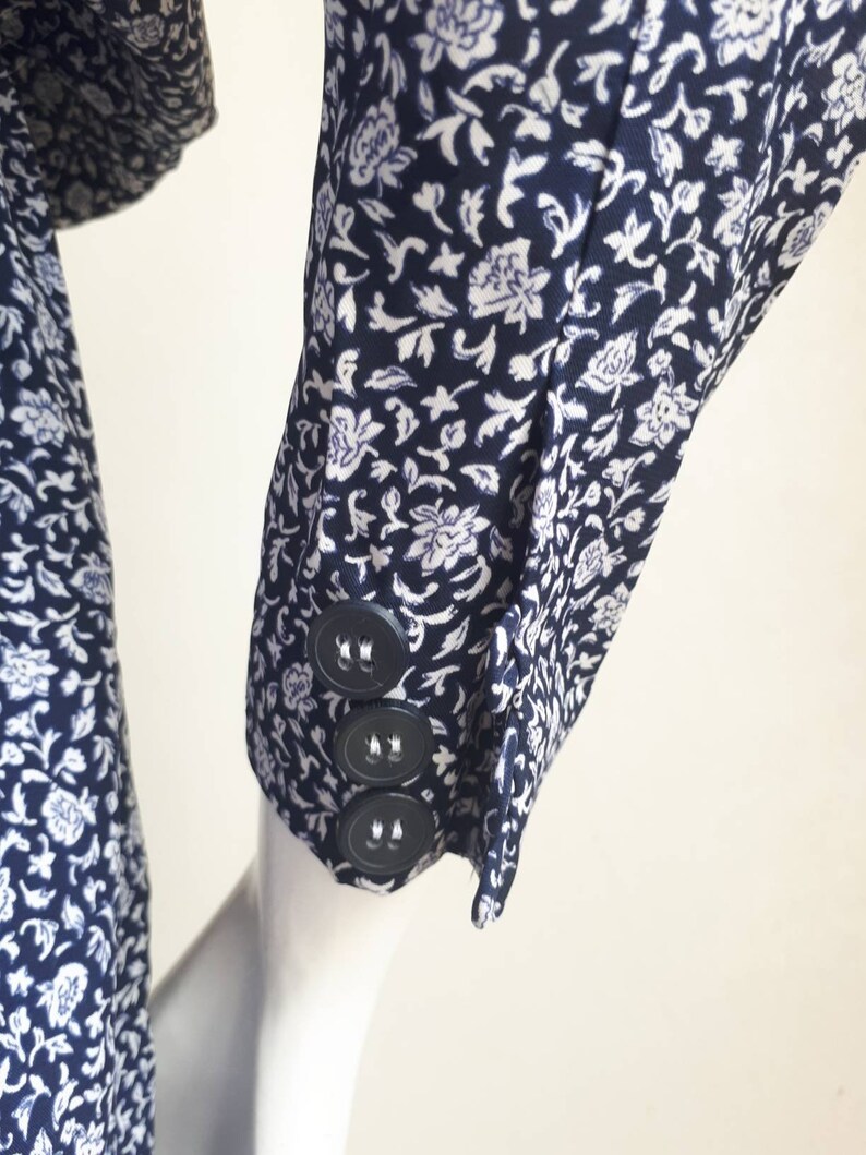 May include: A close-up of a navy blue and white floral patterned shirt sleeve with three black buttons.