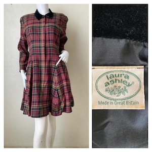 Op de afbeelding: Een vintage rode, zwarte en gouden geruite jurk met een zwarte fluwelen kraag. De jurk heeft lange mouwen en een uitlopende rok. Het label luidt "Laura Ashley Made in Great Britain."
