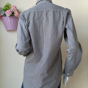May include: A long-sleeved button-down shirt with a black and white gingham pattern. The shirt has a contrasting gray and white gingham pattern on the sleeves.