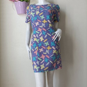 May include: A purple short-sleeved dress with a colorful abstract print of stars, lines, and dashes.