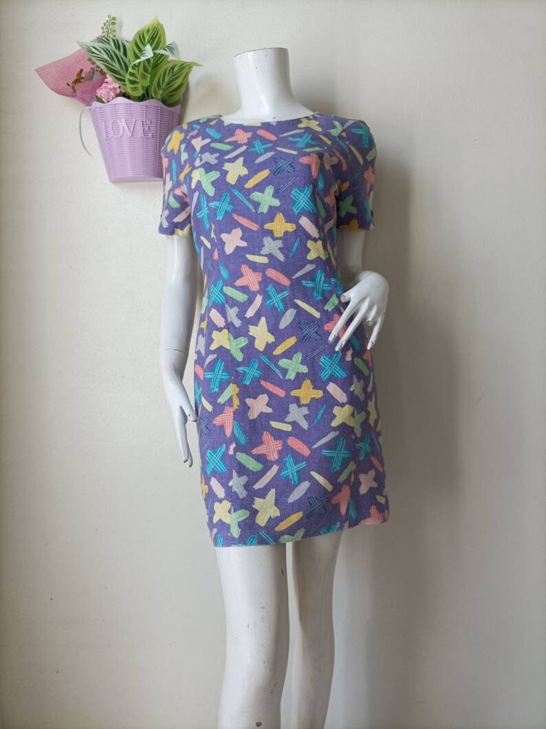 May include: A purple short-sleeved dress with a colorful abstract print of stars, lines, and dashes.