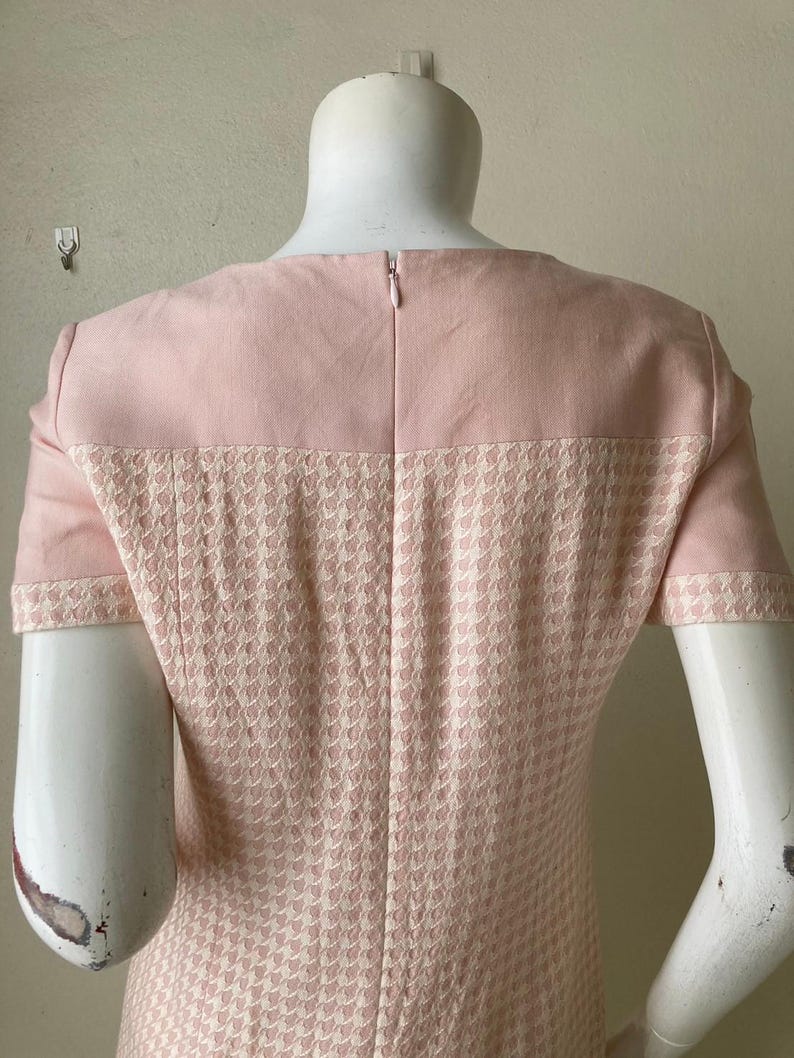 May include: A pink dress with a houndstooth pattern. The dress has short sleeves and a zipper in the back.