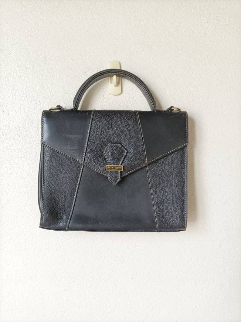 May include: A black leather handbag with a gold clasp and the text "DAUPHINE PARIS" on the front.