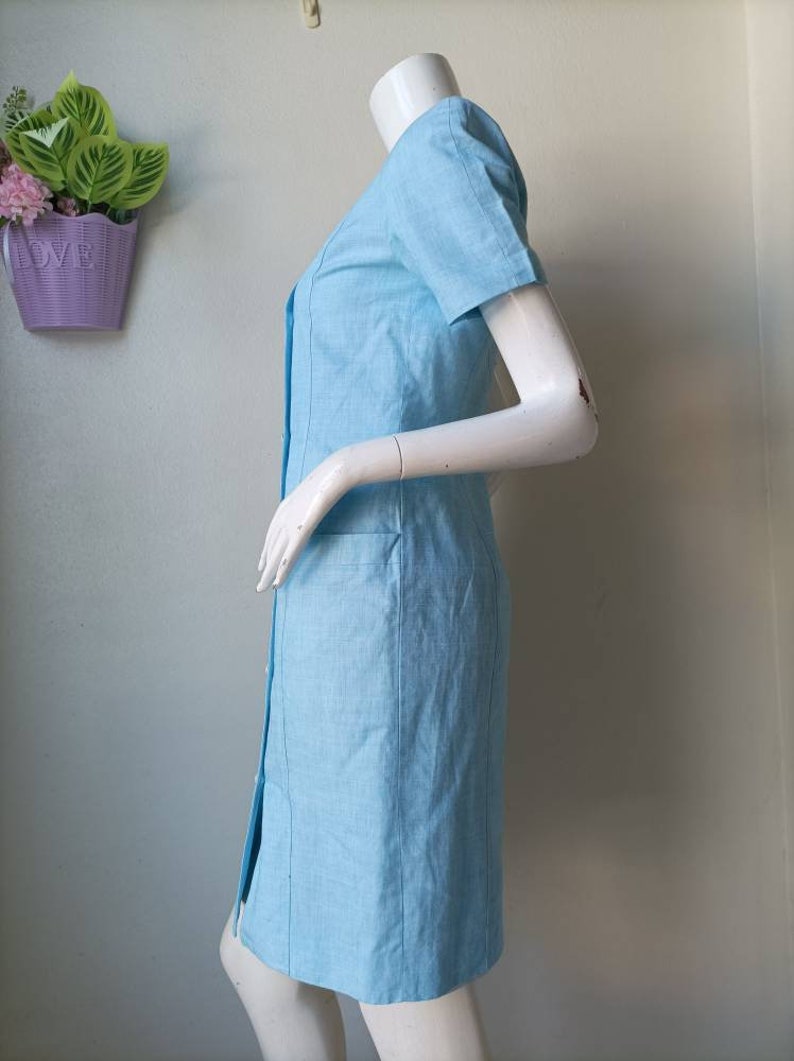 May include: A light blue short-sleeved dress with a button-up front and a pocket on the side.