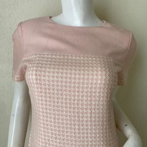 May include: A pink and white short-sleeved dress with a houndstooth pattern. The dress has a solid pink top and a houndstooth bottom.