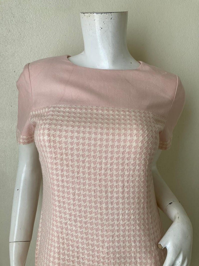 May include: A pink and white short-sleeved dress with a houndstooth pattern. The dress has a solid pink top and a houndstooth bottom.