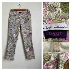 Könnte beinhalten: Hose mit einem Blumenmuster in den Farben Violett, Grün und Weiß. Das Kleidungsstück verfügt über einen Bund mit Knopfverschluss und ein Etikett mit der Aufschrift Sweet Camel und Liberty Art Fabrics. Das Design besteht aus verschiedenen Blumenmotiven.
