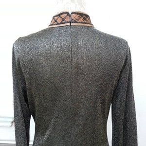 May include: A long-sleeved, metallic gold dress with a black and brown trim around the collar.