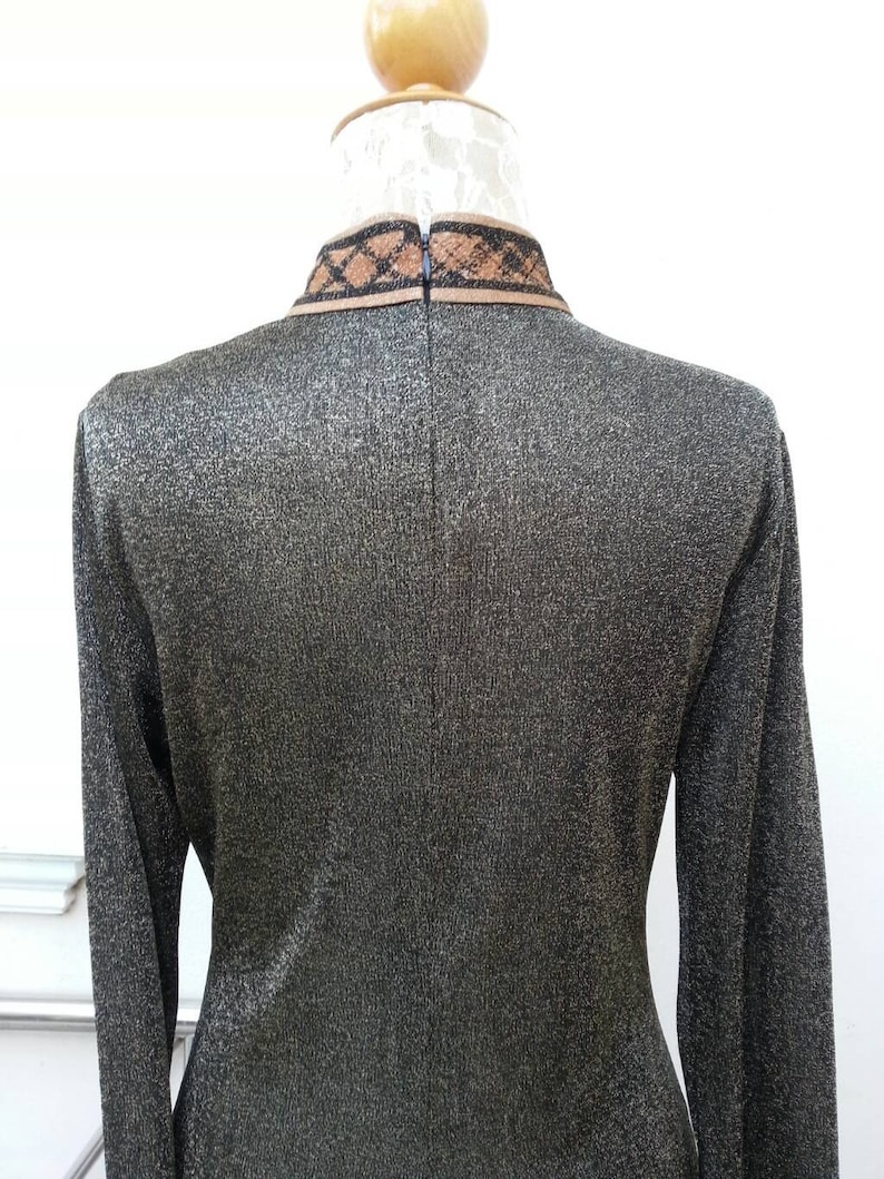 May include: A long-sleeved, metallic gold dress with a black and brown trim around the collar.