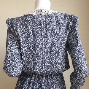 May include: A blue and white floral print dress with a white lace collar. The dress has long sleeves and a fitted waist.
