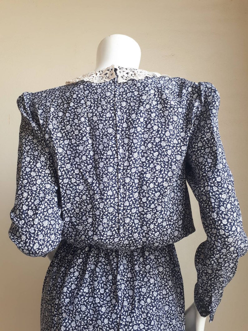 May include: A blue and white floral print dress with a white lace collar. The dress has long sleeves and a fitted waist.