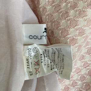 May include: A white tag with black text that reads "courr" and "EF 11AR 0890". The tag has a care label with symbols for washing, drying, and ironing. The tag is attached to a pink and white patterned fabric.