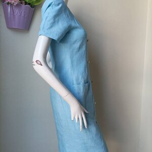 May include: A light blue linen dress with a button-up front and a pocket on the side.