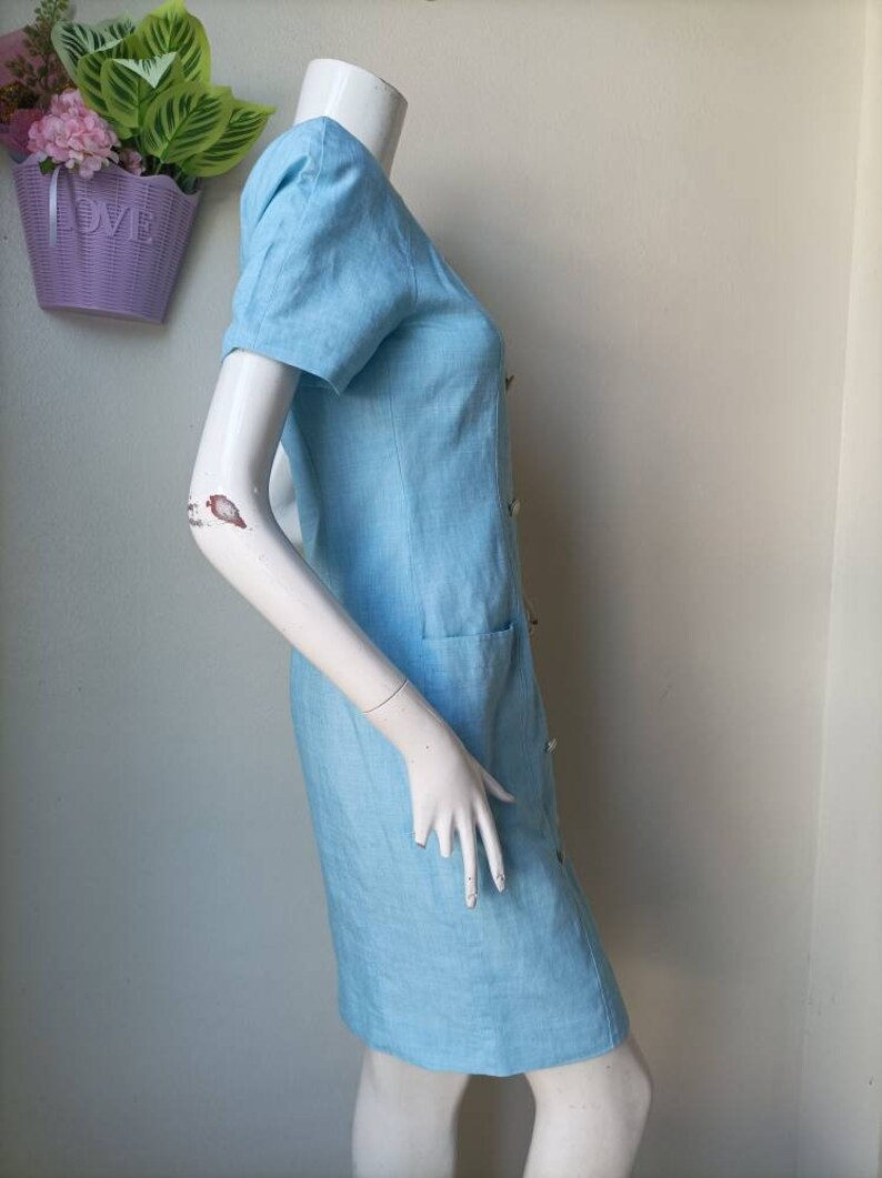 May include: A light blue linen dress with a button-up front and a pocket on the side.
