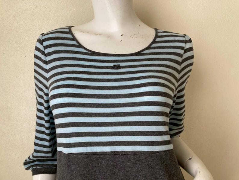 Puede incluir: Vestido a rayas grises y celeste con mangas tres cuartos. El vestido presenta un escote redondo y un corpi&ntilde;o gris oscuro. Un peque&ntilde;o detalle decorativo est&aacute; presente en el escote. El vestido se exhibe en un maniqu&iacute;.