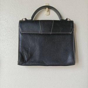 May include: A black leather briefcase with a top handle and a flap closure. The briefcase has a textured surface and a subtle sheen.