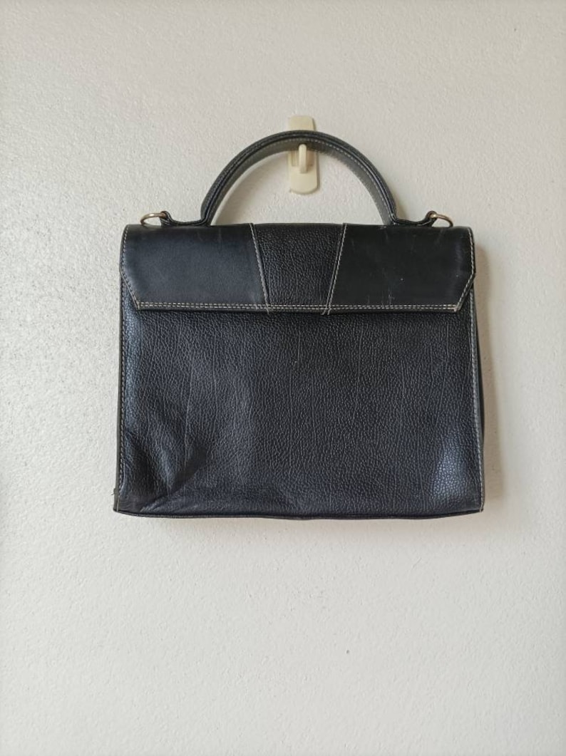May include: A black leather briefcase with a top handle and a flap closure. The briefcase has a textured surface and a subtle sheen.